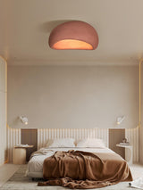 Brick red dome ceiling light above a bed with rumpled bedding and side tables