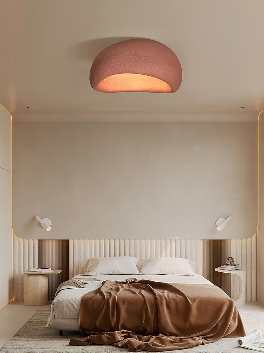 Brick red dome ceiling light above a bed with rumpled bedding and side tables