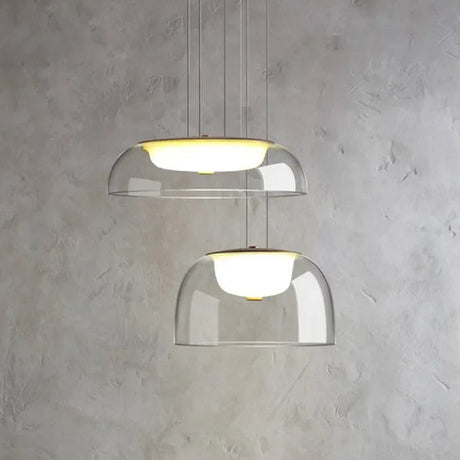 Two clear glass dome pendants lit above a pale marble wall beside a counter