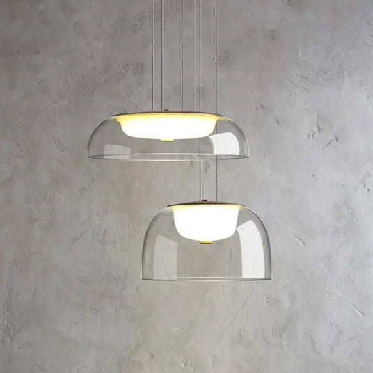Two clear glass dome pendants lit above a pale marble wall beside a counter