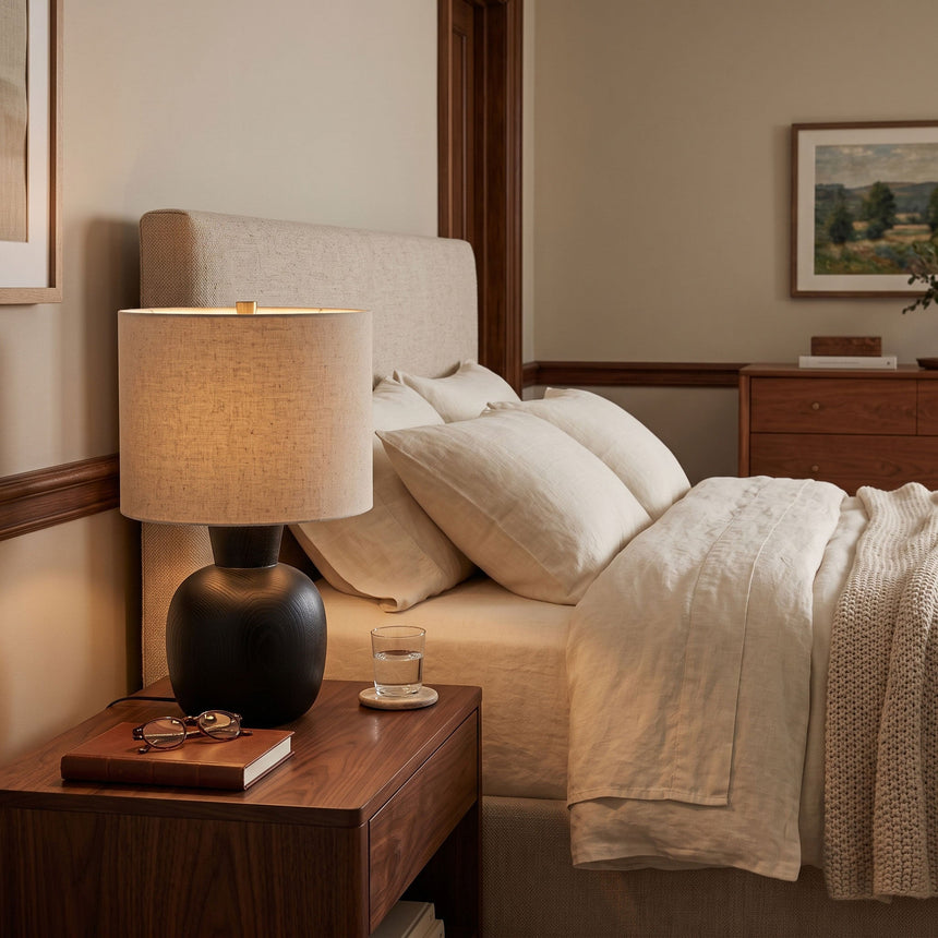 Sphere base lamp lit on a wood nightstand beside a made bed