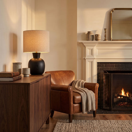 Sphere base lamp lit on a cabinet beside a leather chair and fire