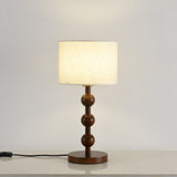 Round table lamp lit against a pale wall, the drum shade glowing