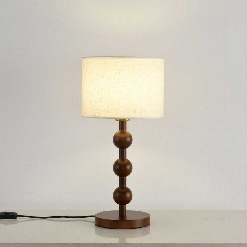 Round table lamp lit against a pale wall, the drum shade glowing