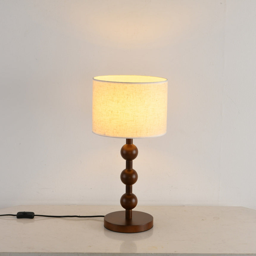 Round table lamp lit close up, the shade bright above the wood spheres