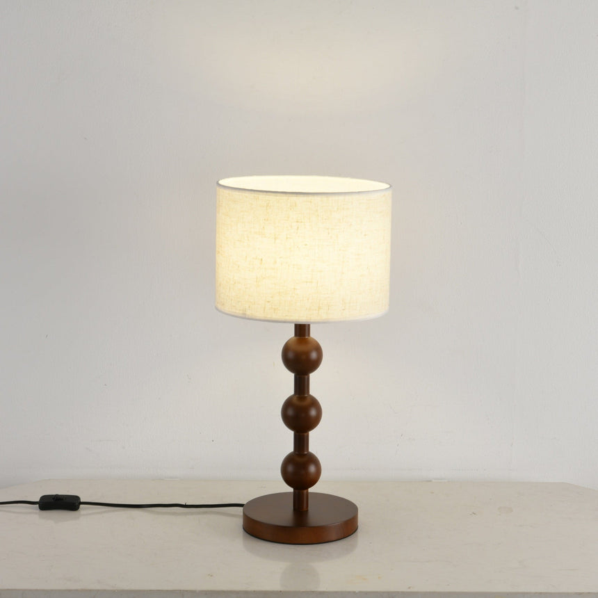 Round table lamp lit and seen at a three quarter angle beside a wall