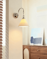 The pleated cone version lit above a walnut dresser beside striped blinds