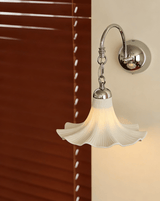 The ruffled shade lit beside red wood blinds, its scalloped edge glowing