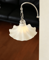 The ruffled shade lit in front of a dark leather sofa and a wood floor