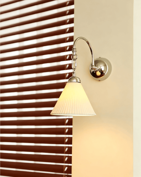 The pleated cone version lit on a pillar beside a window with wood blinds