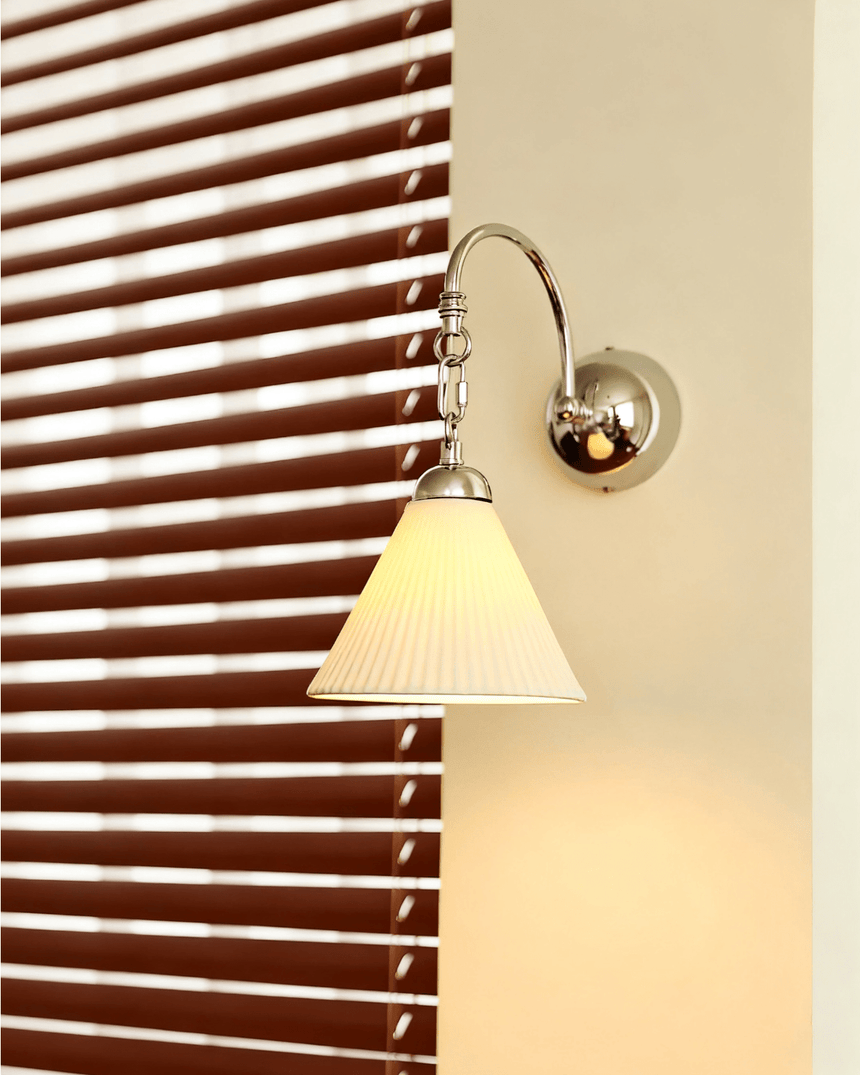 The pleated cone version lit on a pillar beside a window with wood blinds
