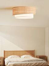 Two tier raffia ceiling light lit above a rattan bed under a sloped ceiling