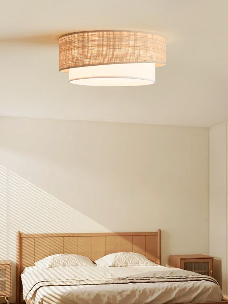 Two tier raffia ceiling light lit above a rattan bed under a sloped ceiling