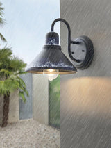 The light lit in the rain on a gray wall beside a gravel path and palms