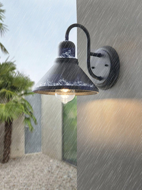 The light lit in the rain on a gray wall beside a gravel path and palms