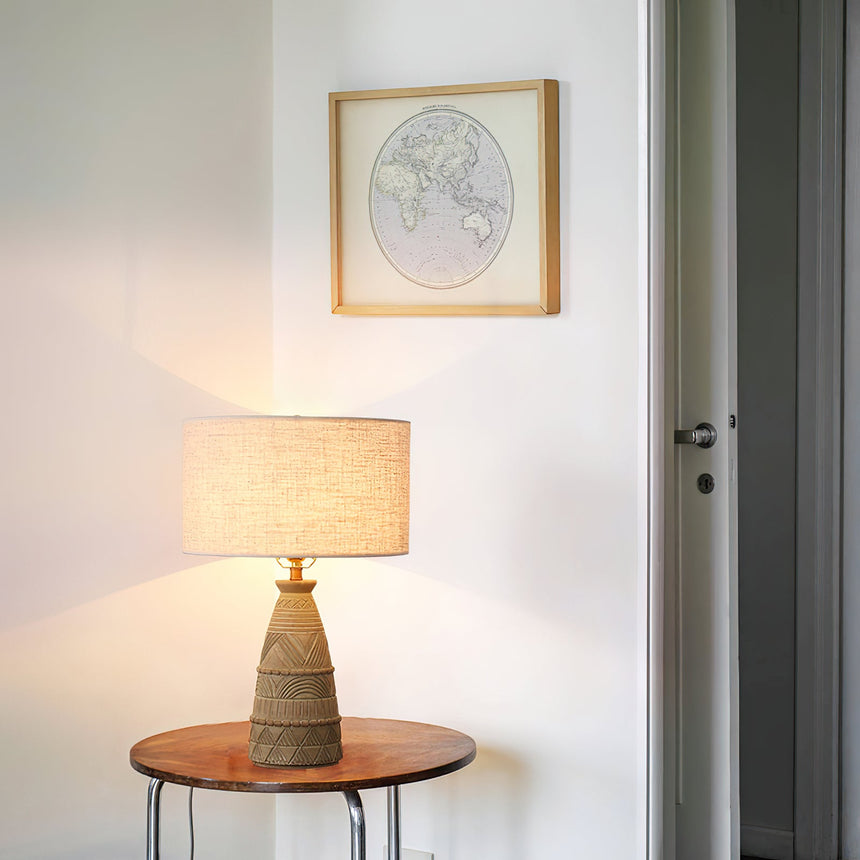 Rustic table lamp lit on a round side table below a framed map print