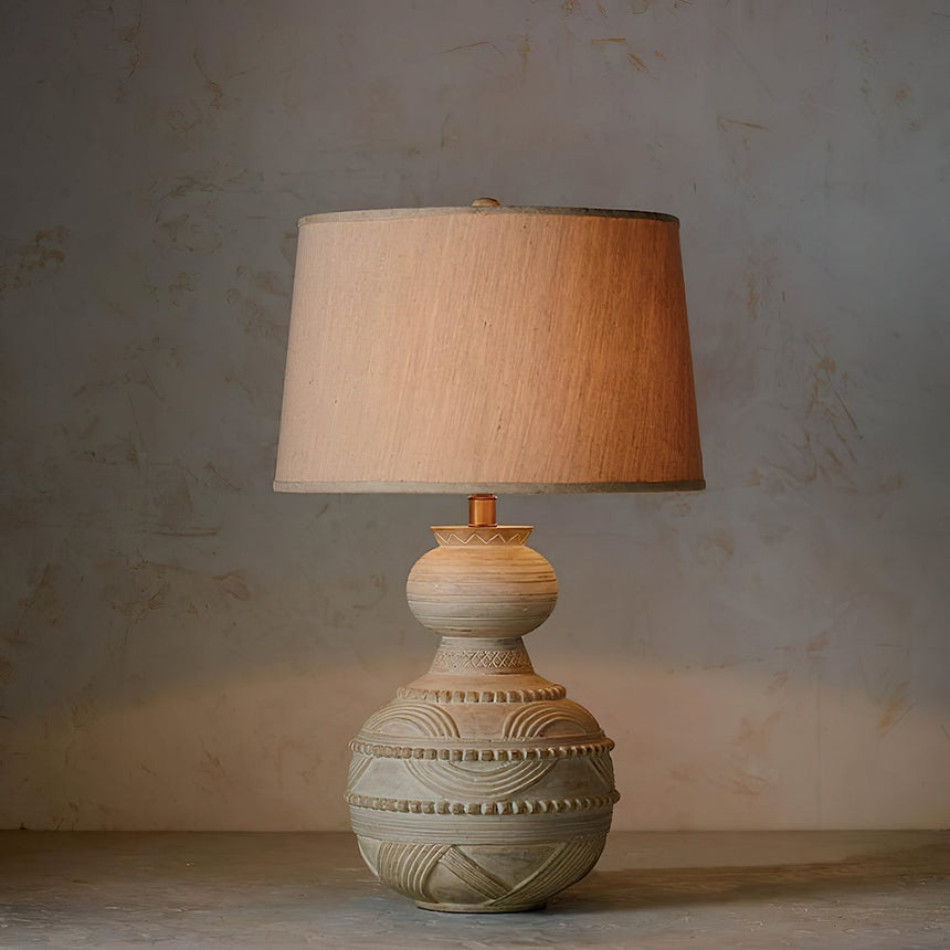 Rounded carved base with banded pattern under a tapered beige shade