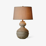 Rustic table lamp with a rounded carved base on a plain white ground