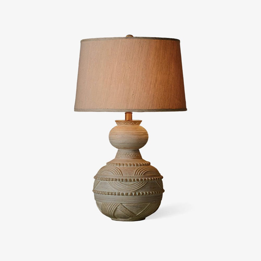 Rustic table lamp with a rounded carved base on a plain white ground