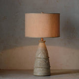 Tapered carved base with chevron bands under a beige drum shade, unlit