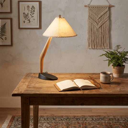 Rustic table lamp lit on a wooden table above an open book and a mug