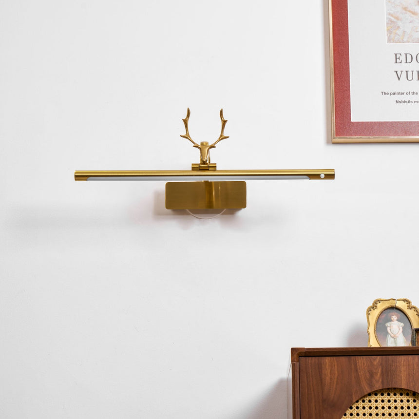 Gold bar lit above a cane fronted dresser with framed pictures and a cup
