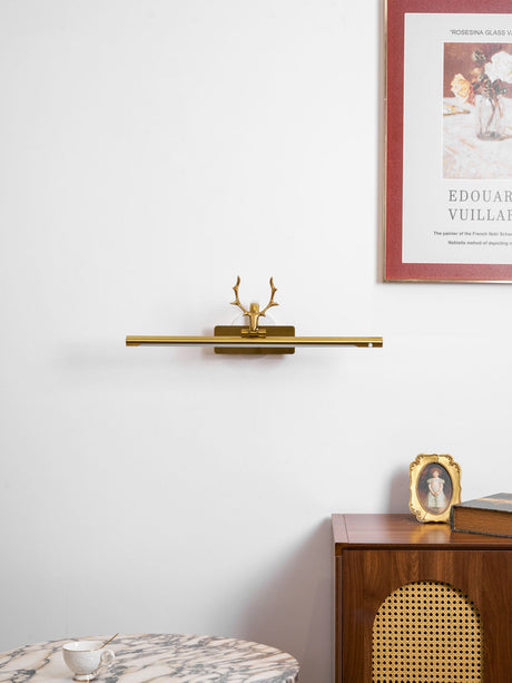 Gold bar lit on a wall of framed prints above a walnut chest with a picture frame