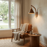 Sconce lit beside a curtained window above an armchair and a stool
