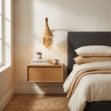 Rustic sconce lit above a wood nightstand beside a bed with pale bedding