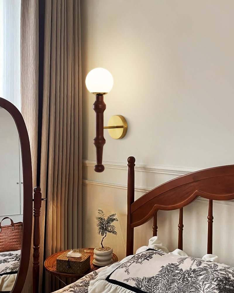 Sconce lit beside a tall spindle headboard and a bedside stack of books