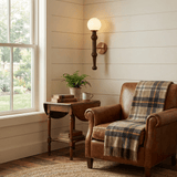 Sconce lit beside a plaid draped armchair and a half round table with a plant