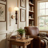 Sconce lit above a side table stacked with books beside a leather armchair