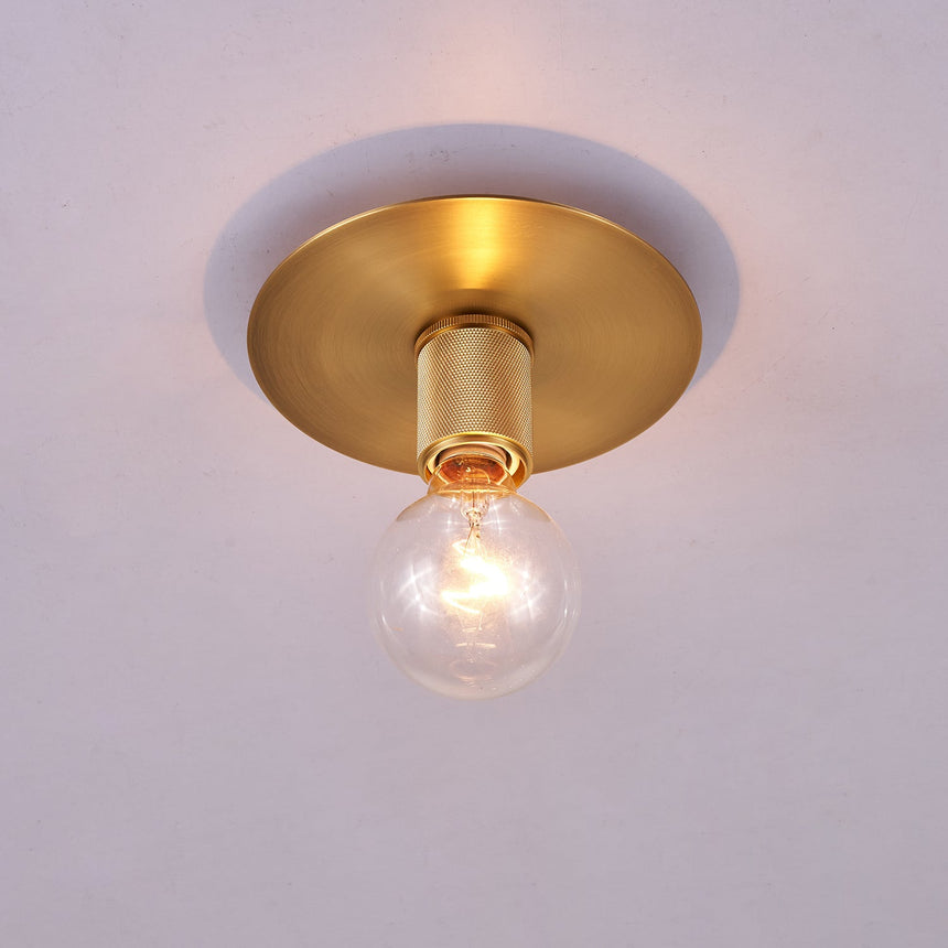 Brushed brass disc ceiling light lit with a clear filament bulb