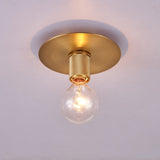 Brushed brass disc ceiling light lit at an angle on a plain ceiling