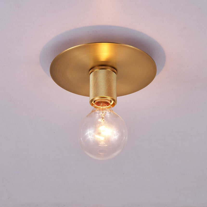 Brushed brass disc ceiling light lit at an angle on a plain ceiling