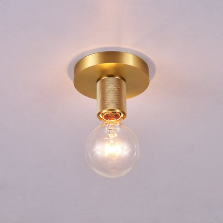Brushed brass disc ceiling light lit and seen close against plaster