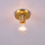 Brushed brass disc ceiling light lit against a pale gray ceiling