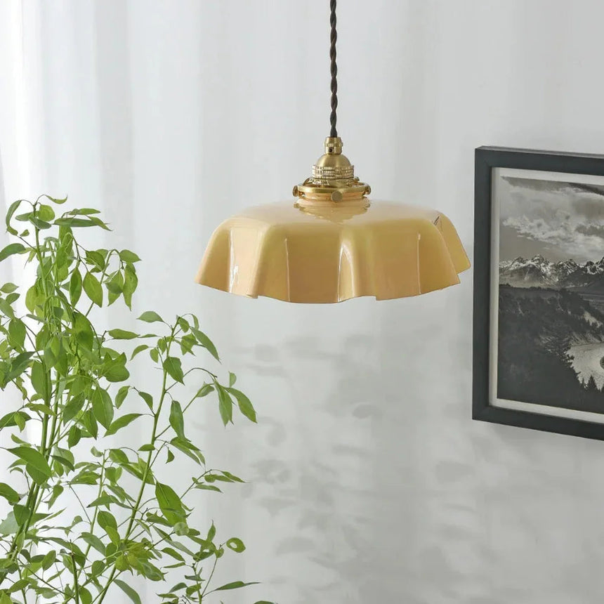 Beige scalloped shade lit beside a trailing green plant and a framed print