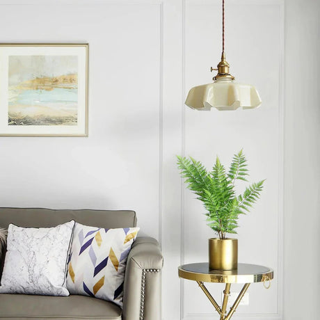 Beige scalloped shade over a gray sofa with a fern on a brass side table