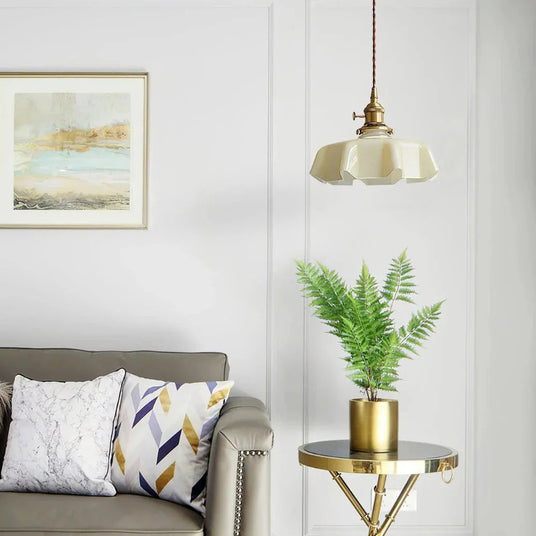 Beige scalloped shade over a gray sofa with a fern on a brass side table