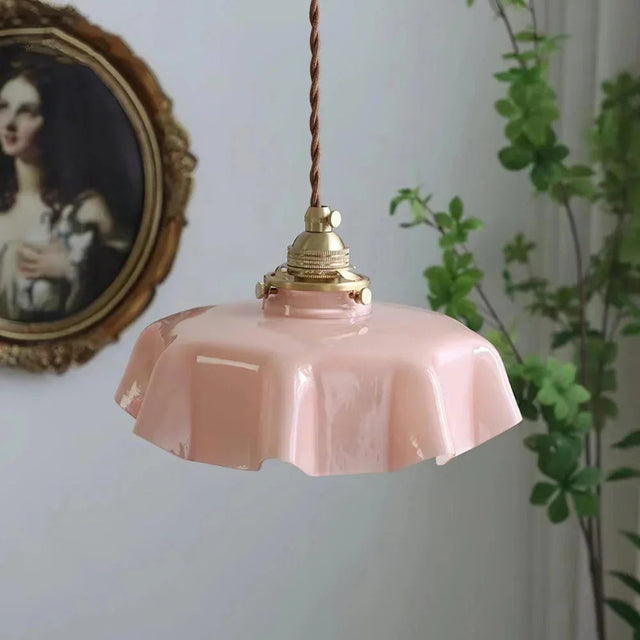 Pink scalloped shade with a brass top beside an oval gilt mirror and ivy