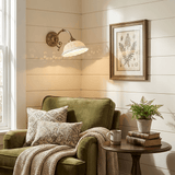 The sconce lit above a green armchair and a small side table with a fern and books