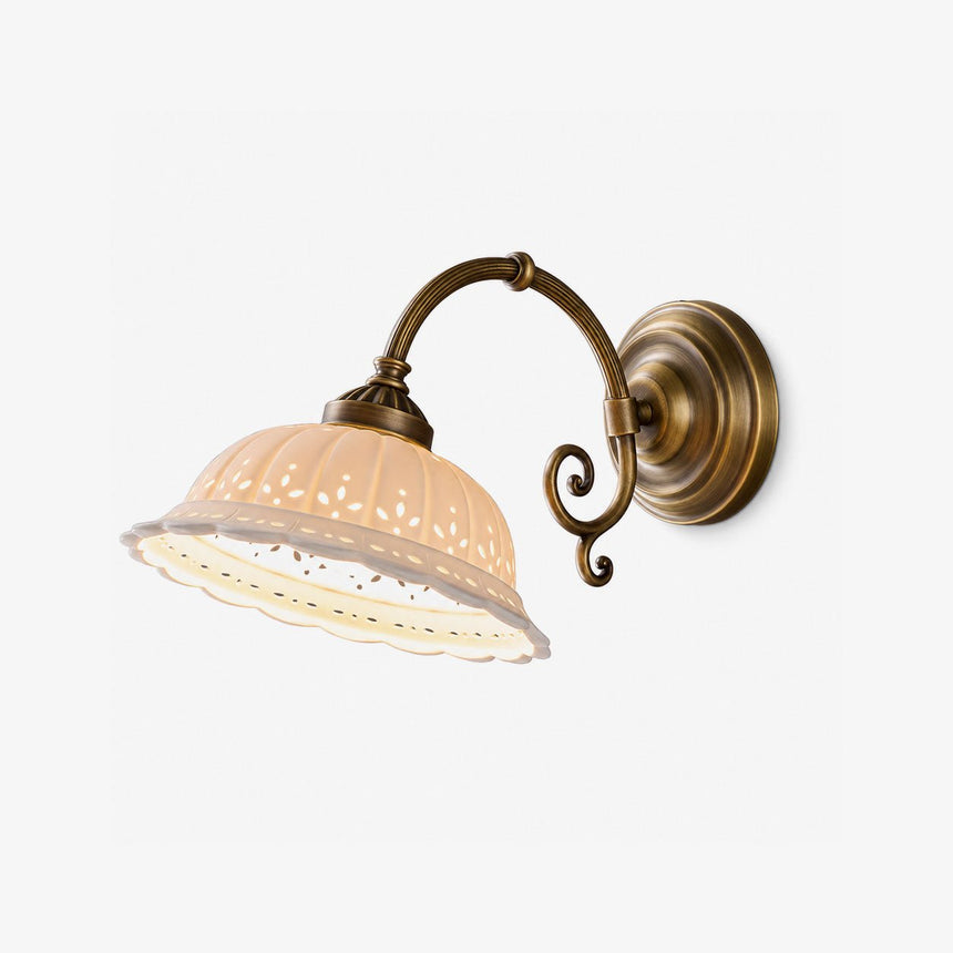 Antique brass wall sconce with a scroll arm and a white pierced ceramic shade with a scalloped edge