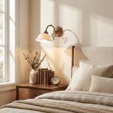 The sconce above a nightstand with books and dried flowers beside an upholstered bed