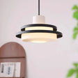 Black stacked disc pendant hung beside a plant on a pale wall