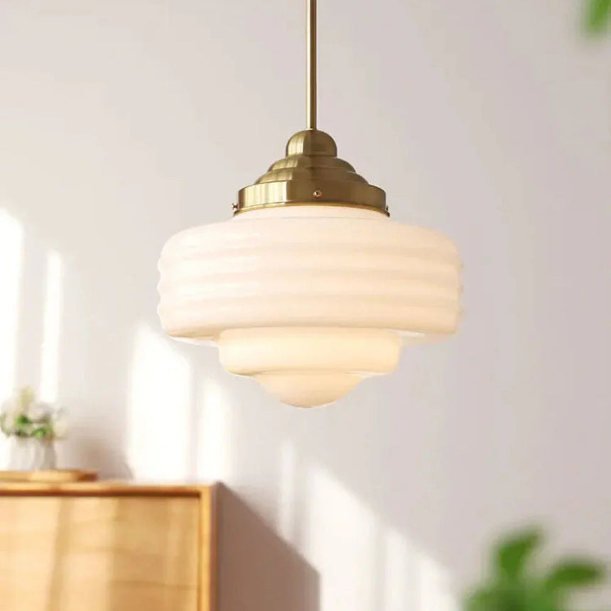 Stepped white opal shade with a brass top hanging above a wooden sideboard