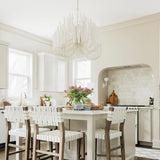Chandelier lit above a kitchen island with stools and open shelving