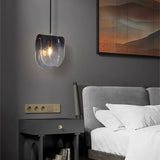 The folded glass shade lit beside a bed above a dark nightstand