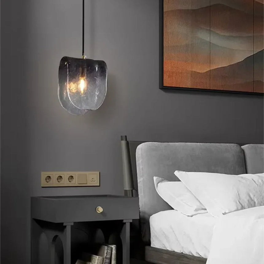 The folded glass shade lit beside a bed above a dark nightstand