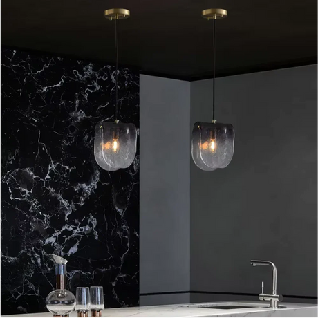 Two folded glass shades lit against a black marble wall above a counter